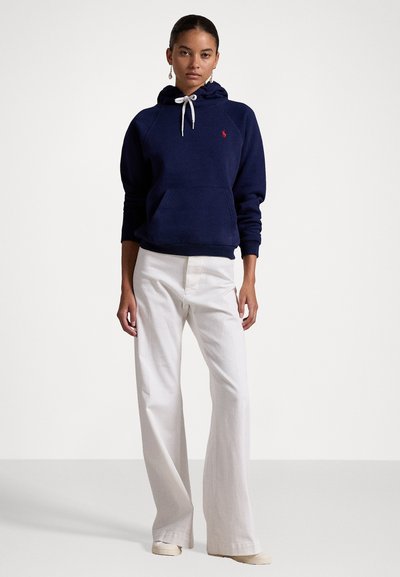 Navyblauwe hoodie met een voorzak, witte trekkoord en een rood logo op de borst, gecombineerd met witte wijde broek.