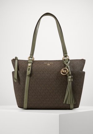 Brązowa i oliwkowo-zielona torba typu tote Michael Kors z złotym logo-kamieniem, ozdobą w postaci chwostu oraz podwójnymi paskami na ramię na białej powierzchni.