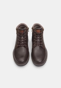 Stivali ankle in pelle marrone con occhielli metallici, chiusura con lacci e cerniere laterali. Dettagli di cuciture a contrasto e fodera interna testurizzata.