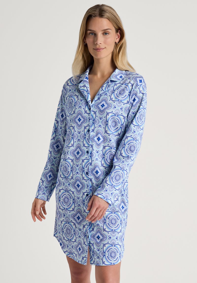Abito camicia azzurro chiaro con un motivo geometrico in blu scuro. Maniche lunghe, colletto, chiusura frontale con bottoni e dettaglio con spacco laterale. Tessuto morbido.