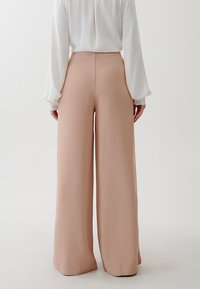 Vida byxor i mjuk rosa tyg, med en slät textur och hög midja. Bakdelen har en ren söm med en diskret dragkedja.