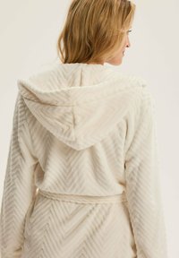 Biała, fakturowana szlafrok z kapturem, z wzorem w jodełkę. Miękka tkanina z paskiem do wiązania w talii.