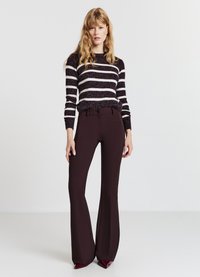 Strickpullover mit dunkelvioletten und weißen Streifen, kombiniert mit maßgeschneiderten, dunkelbraunen Schlaghosen; glatte Textur, figurbetontes Design und ein Knopfdetail.