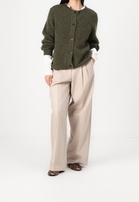 Olive green cardigan z dzianiny z okrągłym dekoltem i zapięciem na guziki, zestawiony z beżowymi spodniami w kant i butami w panterkę.