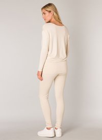 Beige Langarmoberteil und enge Leggings aus weichem Stoff, kombiniert mit weißen Turnschuhen. Das Oberteil hat einen lässigen Schnitt und einen runden Ausschnitt.