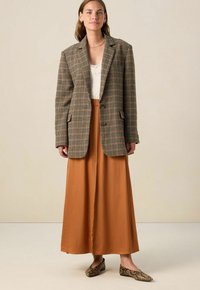 Te grote bruine geruite blazer, crèmekleurige top, roestkleurige maxi rok en schoenen met slangpatroon. De blazer heeft een geknipt revers en twee knopen.