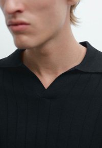 Zwarte gebreide polo met V-hals, voorzien van verticale ribbels en korte mouwen, die een gladde stofuiterlijk toont.