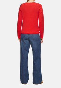 Czerwony sweter z długim rękawem i okrągłym dekoltem, zestawiony z szerokimi niebieskimi dżinsami. Materiał wydaje się miękki; dżinsy mają klasyczną teksturę denimu i przeszycia.