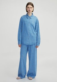 Set di camicia in denim blu chiaro e pantaloni a gamba larga, caratterizzato da ricami di fiori, chiusura con bottoni e colletto a punta. Tessuto morbido.