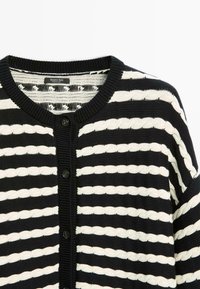 Černobílý pruhovaný cardigan s texturovaným pletením, kulatým výstřihem a zapínáním na knoflíky vpředu. Štítek viditelný uvnitř.