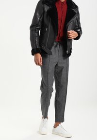 Giubbotto di pelle nera con colletto in pelliccia, camicia a scacchi rossa, pantaloni grigi a sigaretta e sneakers bianche. Il giubbotto ha tasche con zip.