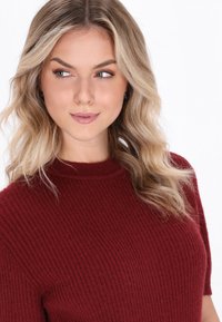 Burgundy ribbattuule sweateri korkealla kauluksella ja lyhyillä hihoilla, jossa on pehmeä rakenne ja istuva siluetti.