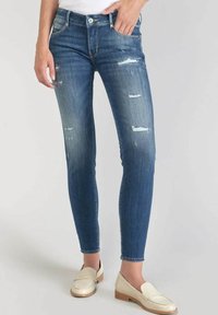 Modré distressed džíny skinny s mnoha slzami a vybledlými vzory, s klasickým pěti kapsovým designem a standardním pasem.