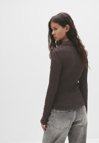 Långärmad, mörkbrun topp i texturerad tyg, åtsittande design och hög krage, kombinerad med något urtvättade grå jeans.