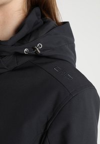 Primer plano de una persona que lleva una chaqueta negra con un cuello alto y un cordón ajustable cerca del cuello.