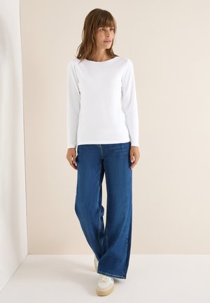 Witte longsleeve top met ronde hals, gecombineerd met wijde blauwe jeans en witte sneakers met beige accenten. Glad textiel.