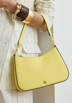 Κίτρινη δερμάτινη τσάντα με χρυσά μεταλλικά στοιχεία, κρατούμενη από άτομο που φοράει κοστούμι με εκρού ρίγες και στρωμένα βραχιολάκια στον καρπό.