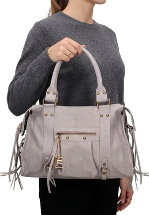 Frau trägt einen grauen Pullover und hält eine hellgraue Lederhandtasche mit vorderer Reißverschlusstasche und goldfarbenen Applikationen.