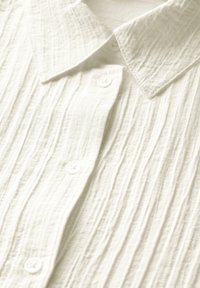 Camicia button-up leggera e strutturata in crema con colletto a punta e bottoni in plastica; presenta sottili pieghe verticali.