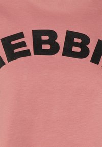 Camiseta de algodón rosa con texto negro en negrita en forma de arco. Tejido suave con una textura lisa, sin patrones ni accesorios adicionales.
