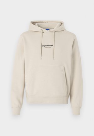 Beige sweatshirt with a hood, front kangaroo pocket, and "Originals Studio" text logo; features long sleeves and ribbed cuffs.