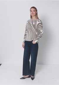 Pull rayé beige et gris avec boutons latéraux, associé à un jean large bleu foncé et des ballerines noires à bout pointu ; texture lisse partout.