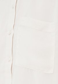 White button-up shirt featuring a pocket on the left side, made of lightweight fabric with a subtle texture. Buttons are white and round.