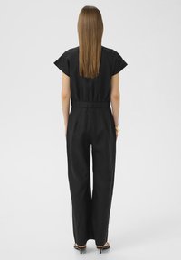 Combinaison en lin noir à manches courtes, taille cintrée et pantalon évasé. Présente une silhouette épurée et une texture lisse.