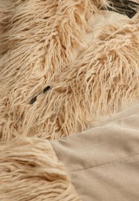 Struktureret beige stof med lange, fluffy fibre sammen med et glat, lyst beige ribbet materiale, med synlige sømme og accenter.