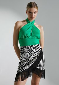 Vestido con cuello halter que presenta una parte superior verde con un corte en forma de lágrima y una falda con estampado de cebra en blanco y negro, con un detalle de flecos en el dobladillo.