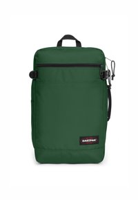 Zaino in nylon verde con forma rettangolare, tasca frontale con zip, manico superiore, tasca laterale e etichetta di marca in basso.