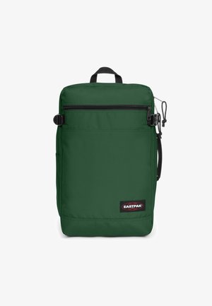 Mochila verde de nailon con forma rectangular, bolsillo frontal con cremallera, asa en la parte superior, bolsillo lateral y etiqueta de marca en la parte inferior.