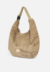 Sac hobo en fausse fourrure beige doux, de forme incurvée, avec une surface texturée et une bandoulière en cuir tan amovible. Comprend un petit détail de tag de marque.