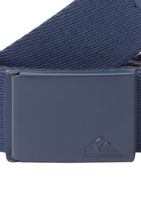 Navy modrý tkaný pásek s obdélníkovou modrou kovovou sponou s logem. Tkanina má texturovaný vzor pro lepší uchopení a odolnost.