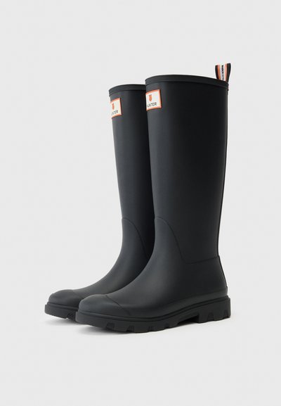 Crne gumene čizme do koljena s glatkom teksturom, okruglim vrhom, čvrstim potplatom i narančastom oznakom branda na nogavici.