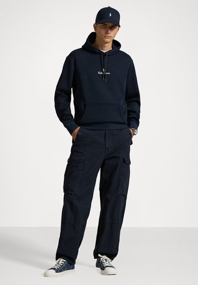 Sudadera marina con cordón y bolsillo frontal, combinada con pantalones cargo marinos con bolsillos laterales y un ajuste relajado. Zapatillas blancas.