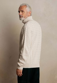 Sweter w kolorze kremowym, o dzianinowym splotcie, z wysokim kołnierzem, ozdobiony wypukłym wzorem w warkocze oraz ściągaczami na rękawach i u dołu.