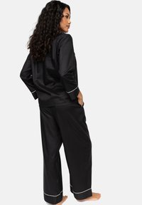 Conjunto de pijama negro que incluye una camiseta de manga larga y pantalones holgados, adornado con ribetes blancos en los puños y el dobladillo para resaltar el contraste.