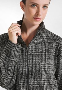 Svart och vit zip-up jacka med en texturerad, vävd mönster. Har hög krage och en slank dragkedjedetalj. Mjukt tyg.