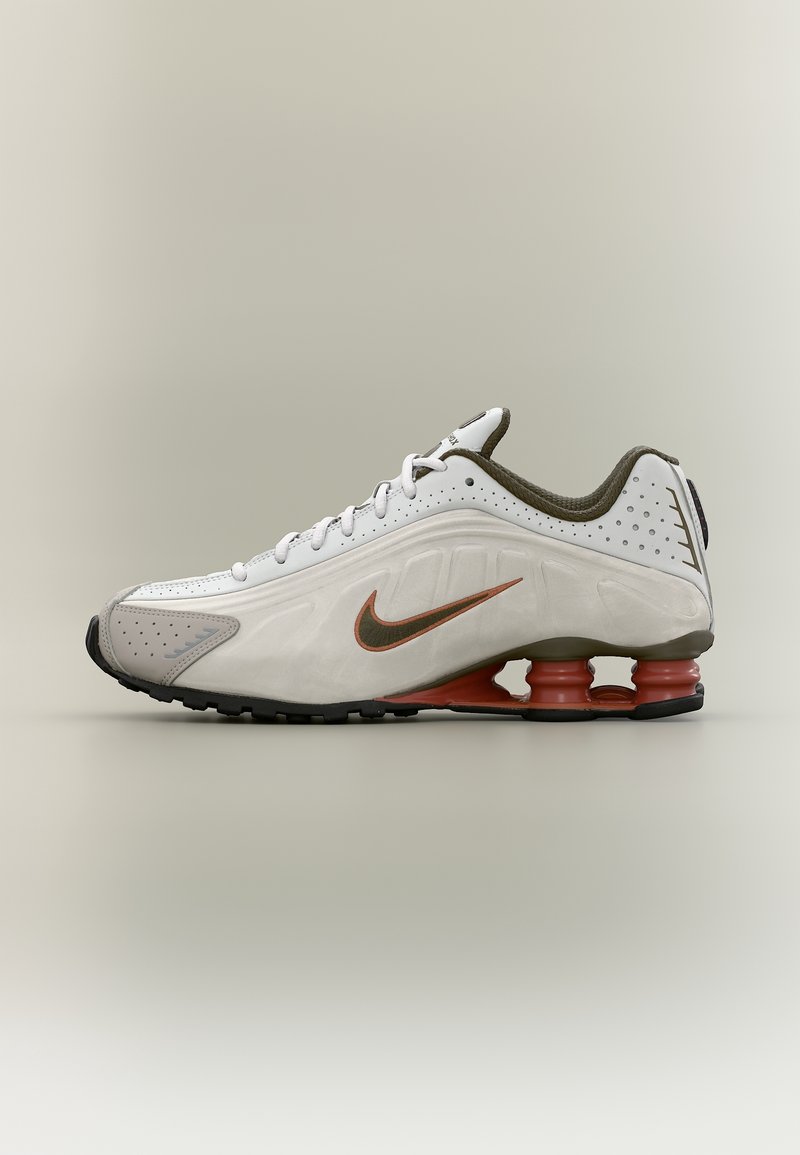 Baskets Nike blanches et grises avec un design à lacets, logo Swoosh marron, détails perforés et semelles uniques à absorbeurs de chocs semblables à des ressorts.