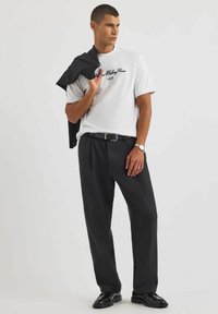 Biała koszulka krótki rękaw z czarnym napisem, w połączeniu z luźnymi czarnymi spodniami i czarnymi butami. Czarna kurtka zarzucona na jedno ramię.