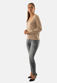 Maglione beige a V con maniche lunghe, tessuto a maglia. Abbinato a jeans slim-fit grigio chiaro e tacchi a spillo neri. Nessun motivo visibile.