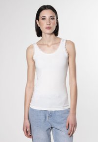 Weißes Tanktop mit Spitzenbesatz am Ausschnitt und den Trägern, aus einem glatten, leichten Stoff, kombiniert mit ausgewaschenen blauen Jeans.