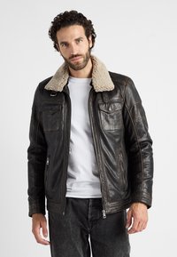 Bruine leren jas met een crème faux shearling kraag, ritssluiting aan de voorkant en twee borstzakken. Heeft een gestructureerde afwerking en een getailleerd ontwerp.