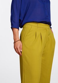 Blauwe, kortärmige blouse met knoopsluiting; olijfgroene plissé broek; gladde stoftextuur; accentueert met een eenvoudige armband.
