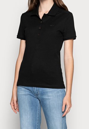 Femme portant un polo noir cintré à manches courtes avec des boutons, associé à un jean bleu clair.