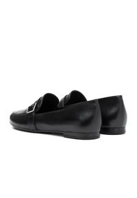 Zwarte leren instaploafers met een zilveren gespdetails op de bovenkant, lage platte zool, weergegeven vanuit een achterzijde hoek.
