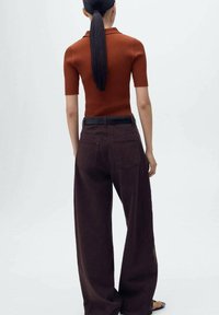 Haut orange côtelé à manches courtes associé à un pantalon large marron foncé. La tenue présente une coupe ajustée et une ceinture noire à la taille.