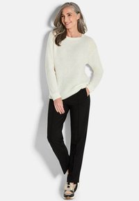 Cremefarbener, strukturierter Strickpullover mit Rautenmuster, kombiniert mit schwarzen, maßgeschneiderten Hosen und mehrfarbigen Sneakers. Lässige Passform und entspanntes Design.