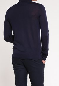 Pull bleu marine avec col polo, manches longues et silhouette ajustée. Confectionné en tissu léger avec une texture lisse.